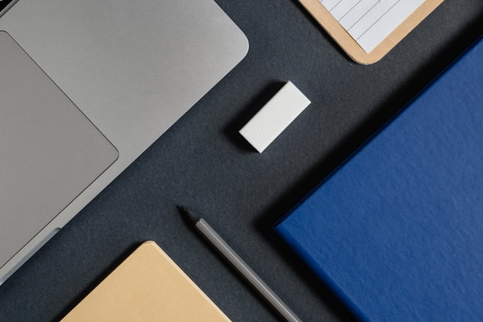 Flat lay of a modern workspace with a laptop, notepads, pen, and eraser on a dark background.