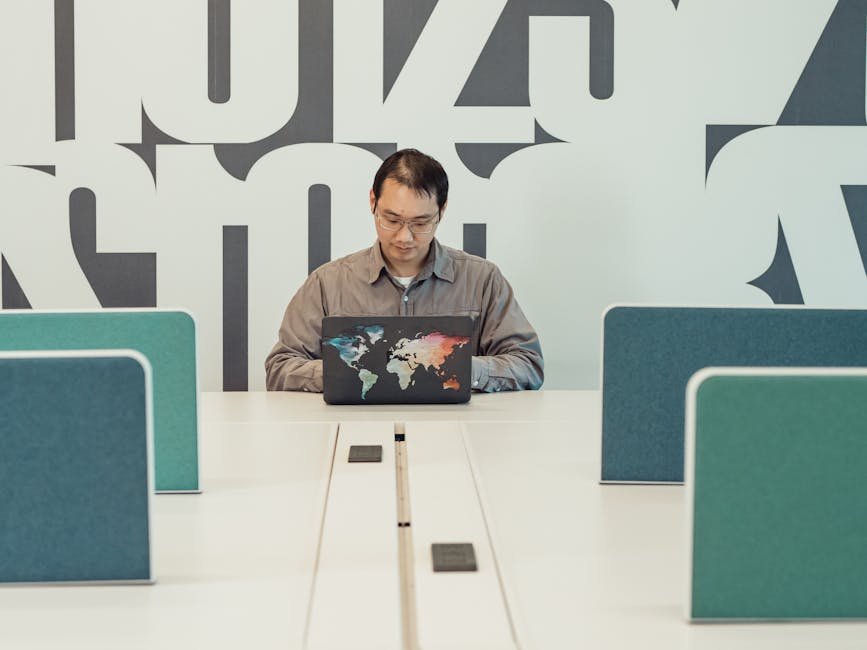 Asian man working on laptop in contemporary open office space with abstract wall design.