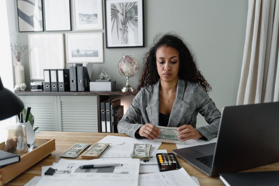 Focused woman counts cash at desk surrounded by office items, emphasizing finance and professionalism.