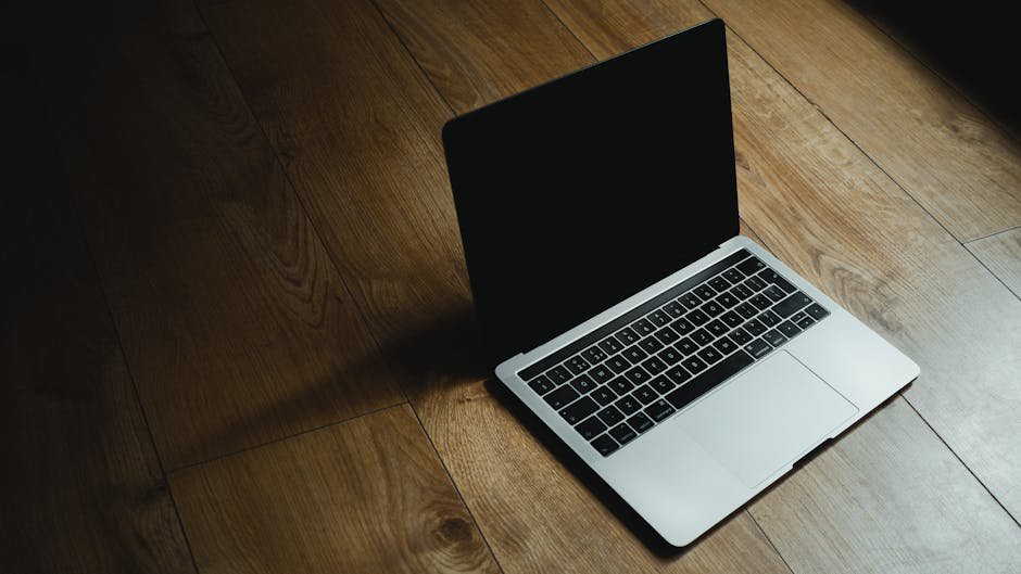 MacBook placed diagonally on a warm wooden floor with soft lighting.