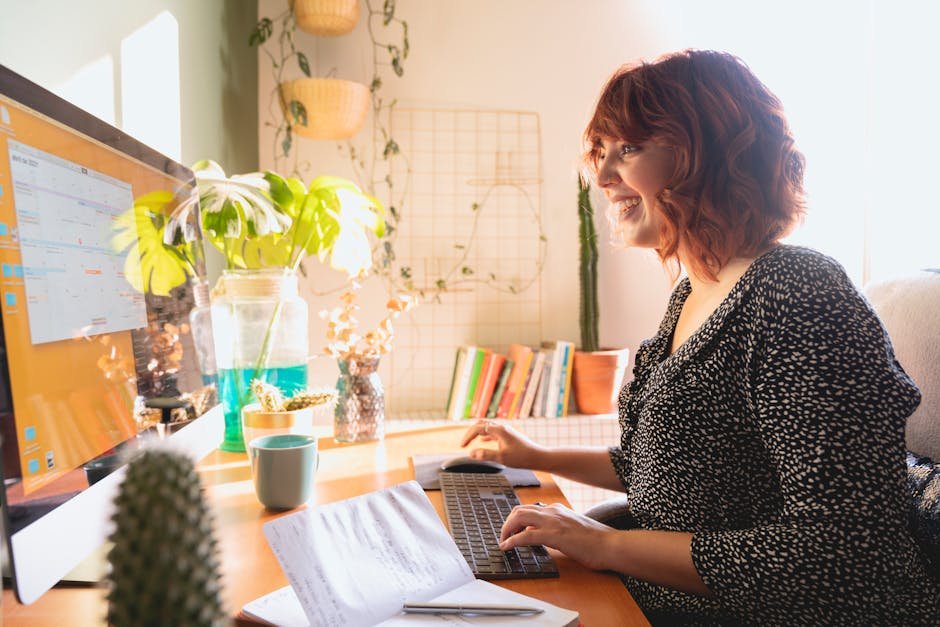 Woman comfortably working from home with plants on a sunny desk, showcasing modern technology.