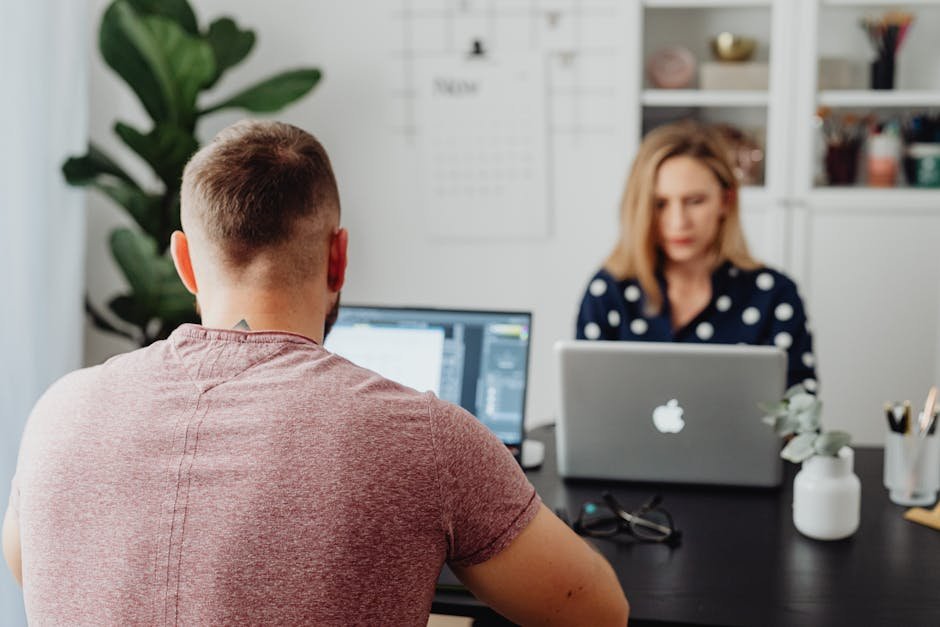 Two professionals working on laptops in a modern office setting.