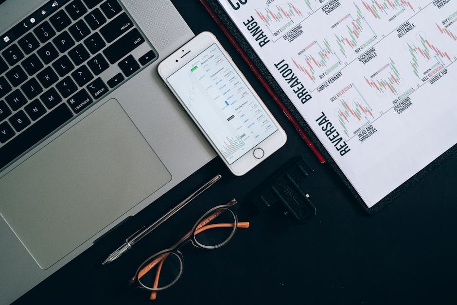 Laptop, smartphone, and financial charts on office desk for market analysis.