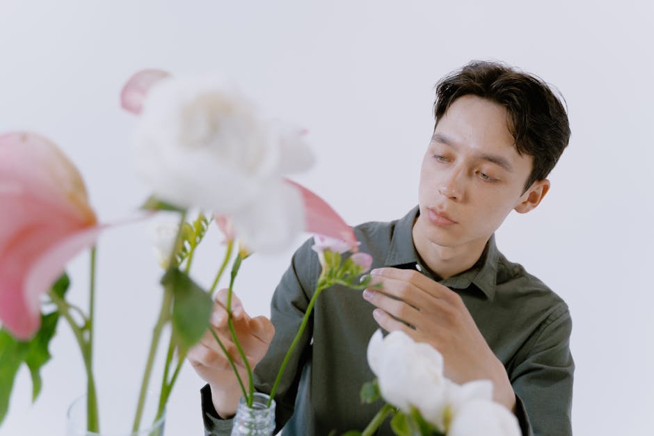A man in a gray shirt attentively arranging flowers in a bright, minimalist indoor setting.